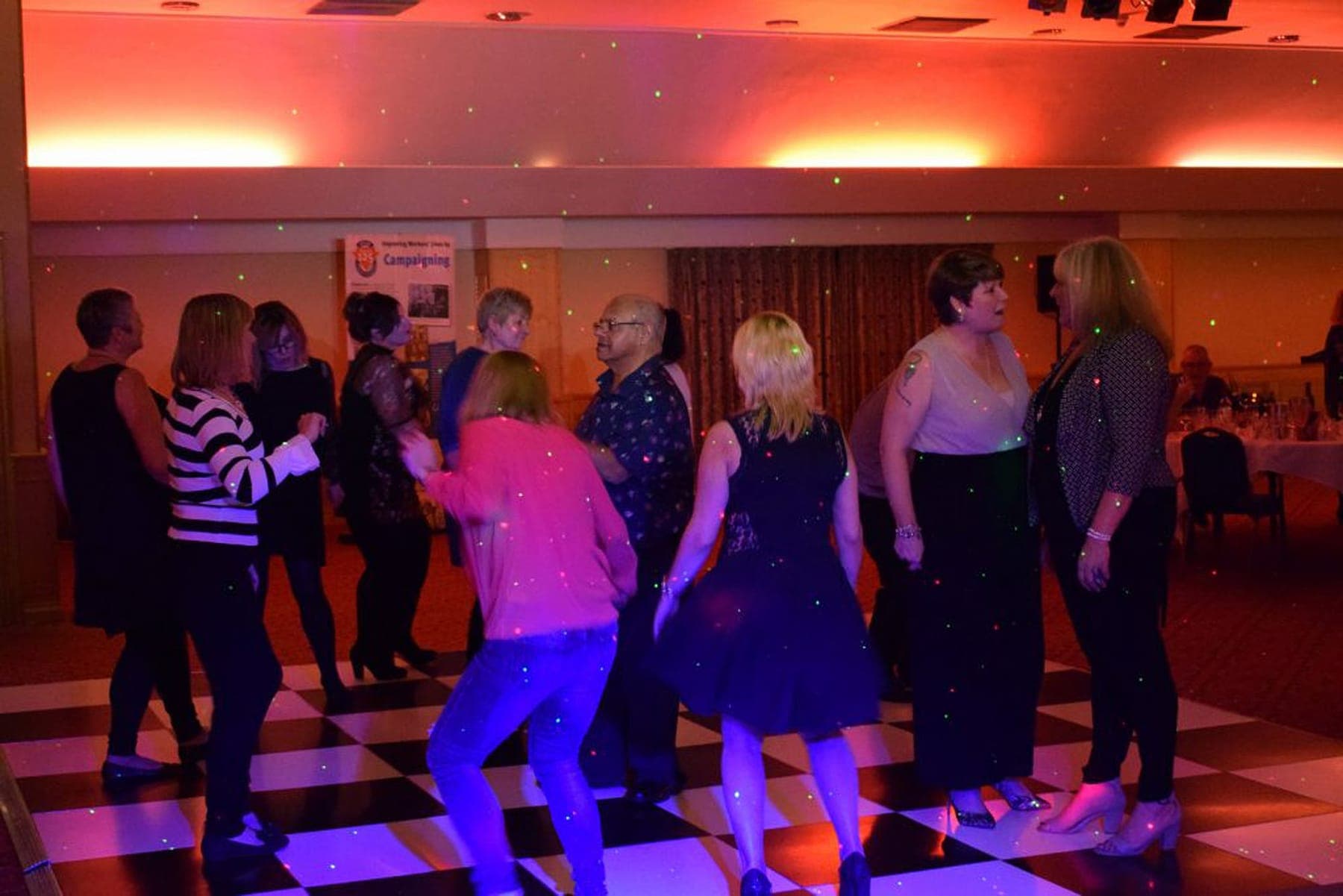 A busy function-room dance floor on a lit chequerboard floor
