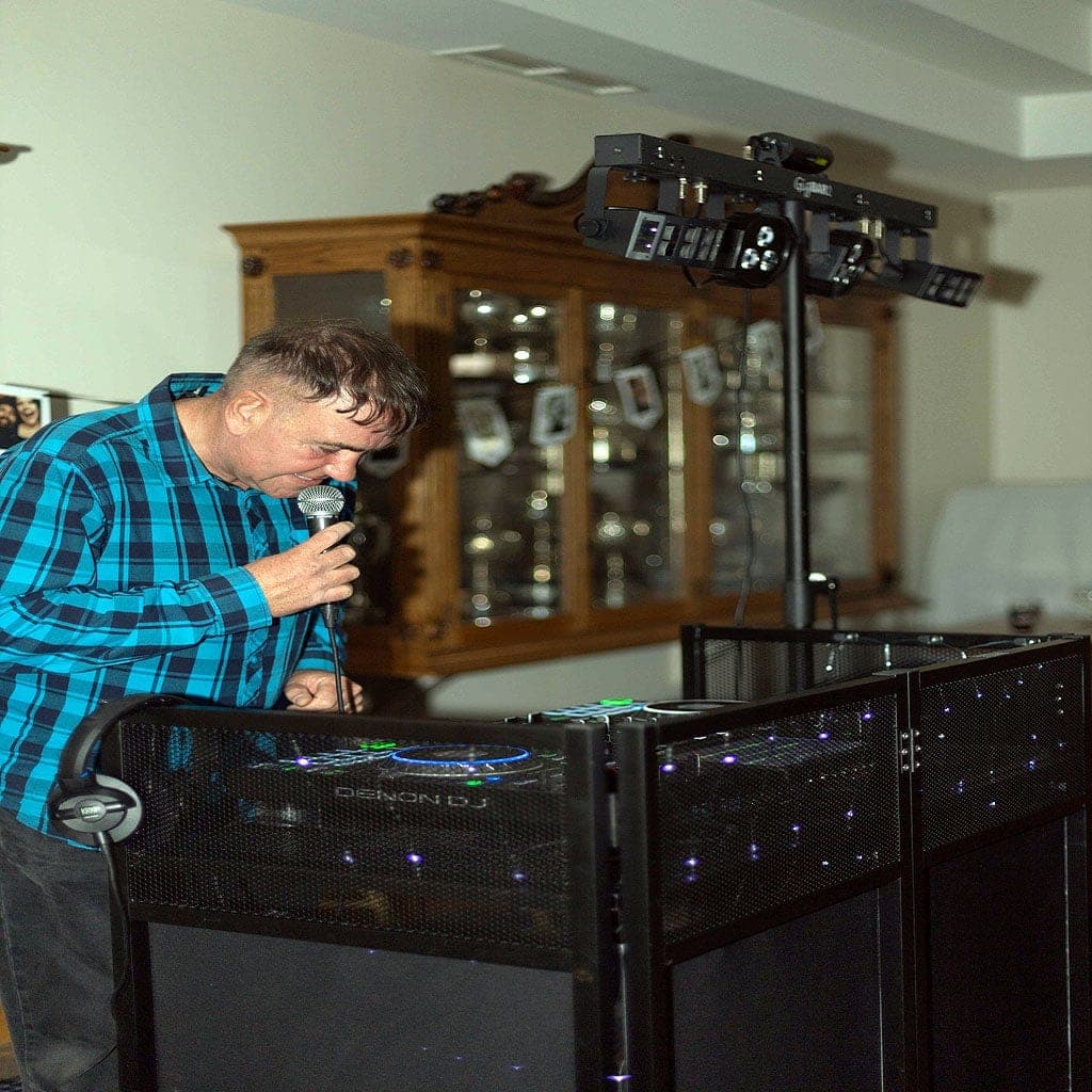 A DJ singing into a microphone behind a lit DJ booth