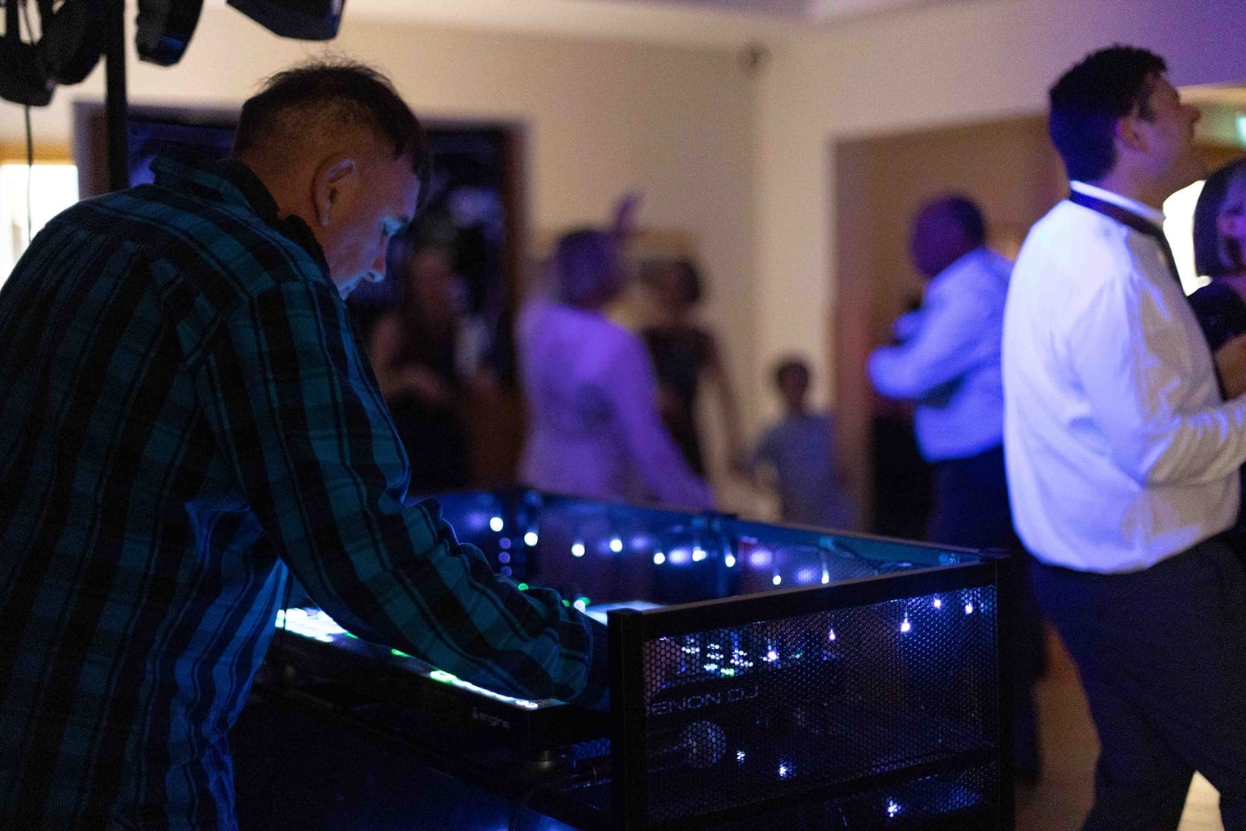 A DJ working the decks at a wedding reception while guests dance behind