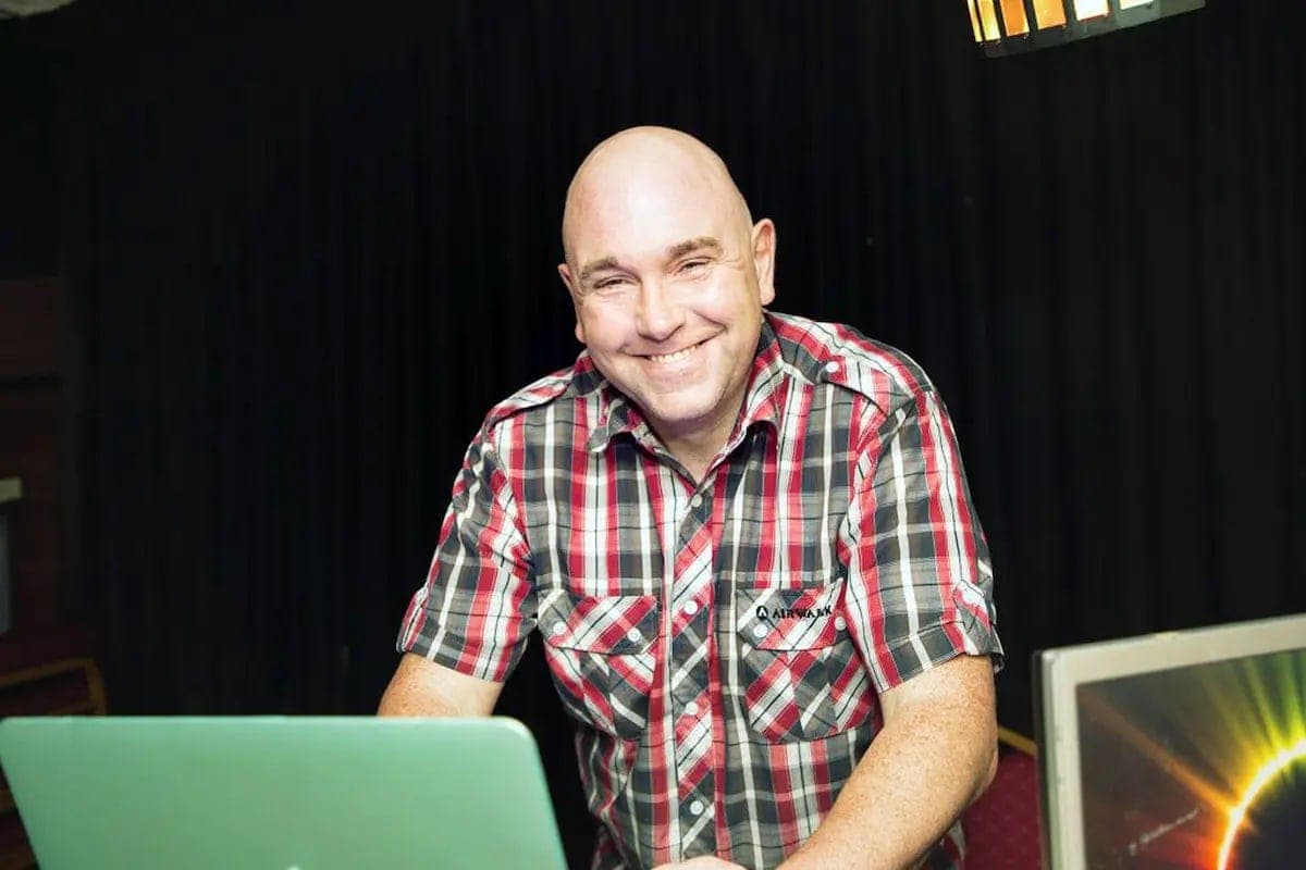DJ Sime smiling behind a laptop at a gig